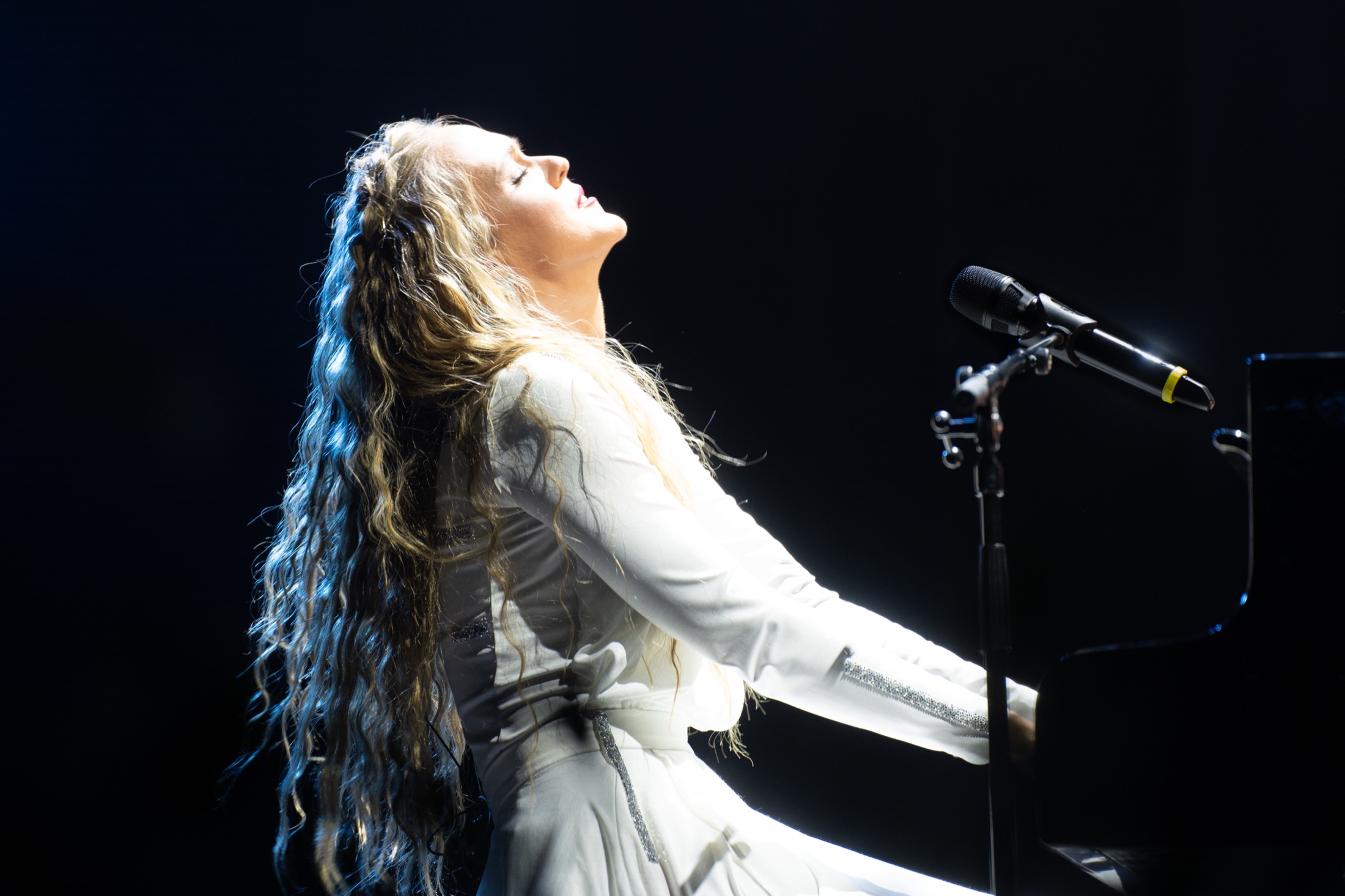 Kadri Voorand leaning back at the piano in a stage spotlight.